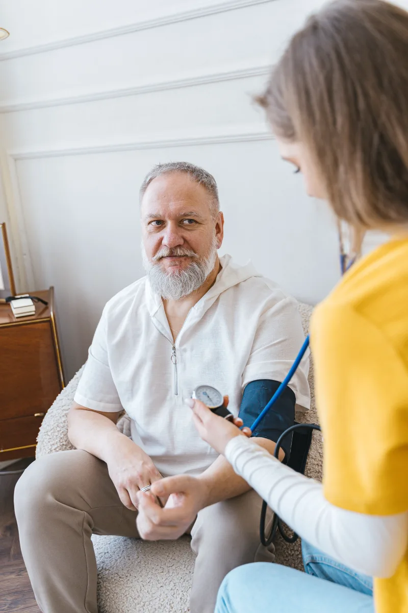 Healthcare worker in yellow scrubs checking an older man's blood pressure in a bright home