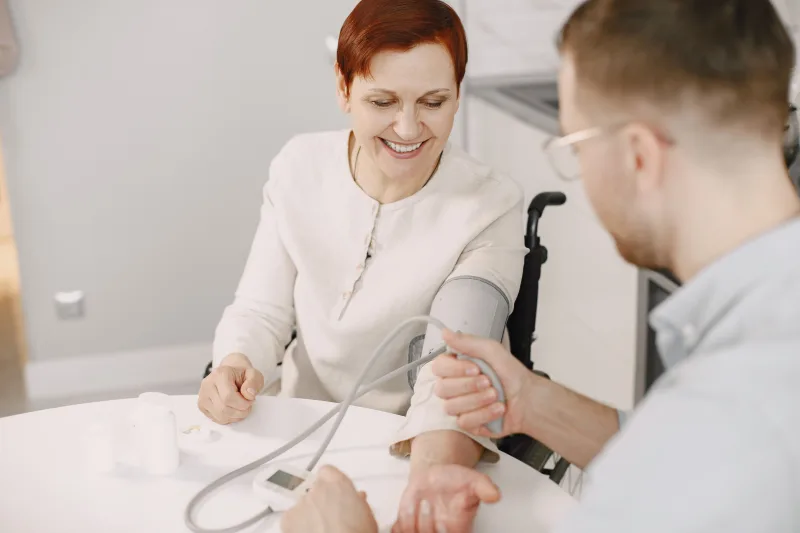 Healthcare worker measuring an older woman's blood pressure at a table