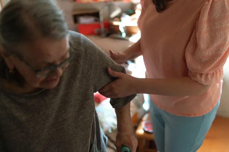 Caregiver supporting an older woman as she moves indoors